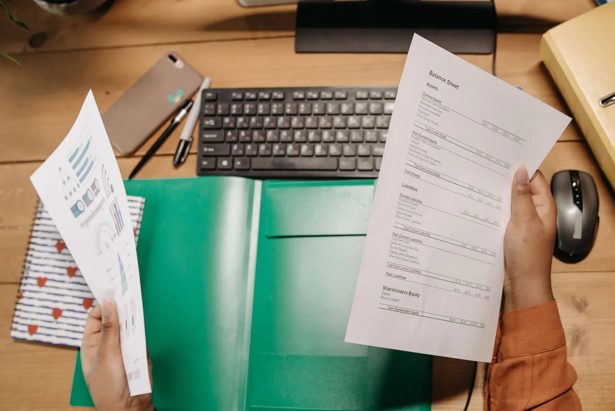 Business owner holding a loan statement in one hand and a financial report in the other at a timber desk, comparing figures